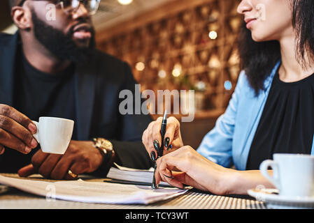 Cheerful businessman and businesswoman have lunch at restaurant, sitting at table, drinking coffee, discussing project. They are looking at each other Stock Photo