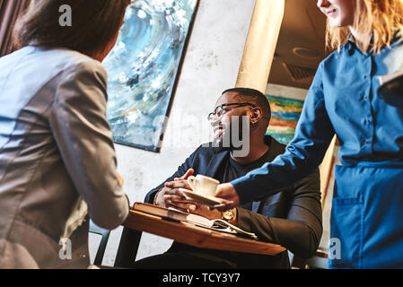 African american businessman and caucasian businesswoman having business lunch at restaurant, sitting at table near window, discussing project, smilin Stock Photo