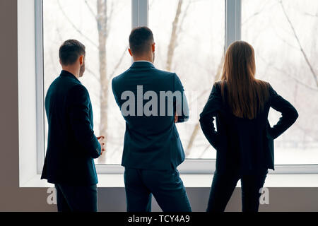 Back view of business people talking during the coffee break stand near the window in office. Business team Stock Photo