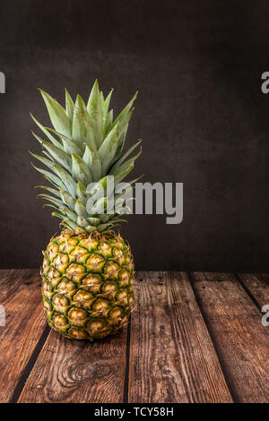 Pineapple Fruit photographed on a wooden table against a black slate background. Stock Photo