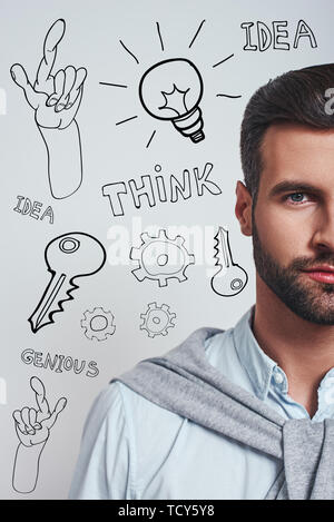 Full of ideas. Vertical half face portrait of a confident bearded man in blue shirt looking at camera while standing against grey background with diff Stock Photo
