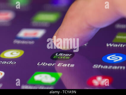 Finger pressing Uber Eats icon to load the app on a touchscreen on a smartphone or tablet mobile device. Stock Photo