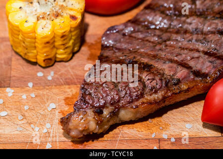 Close up freshly grilled steak on wood with tomatoes and corn Stock Photo