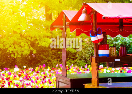 Stall with traditional Dutch symbols in national colors photographed against sunset light with blurred tulips in the background. Traditional Holland wooden shoes. Netherlands, abstract concept. Stock Photo