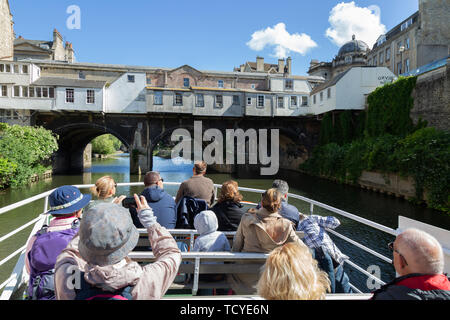 Bath England - a tourist boat with people approaching Pulteney Bridge on the River Avon in summer; UNESCO world heritage site, Bath Somerset UK Stock Photo