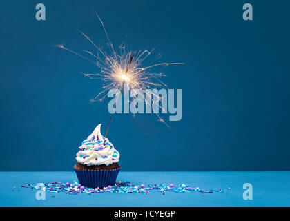 Birthday Cupcake with sparkler against a blue background. Stock Photo