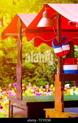 Stand with traditional Holland symbols in national colors taken against sunset light. Blurred colorful tulips in the background. Traditional Dutch wooden clogs. Netherlands, abstract concept, travel. Stock Photo