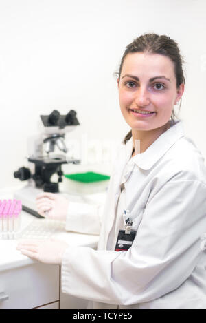 Female researcher smiling. Female researcher using microscope and smiling at camera in the laboratory . Stock Photo