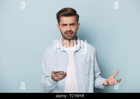 Angry man holding smart phone looking at camera studio shot Stock Photo