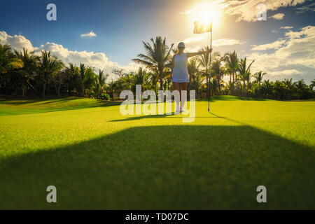 Young woman golfer standing on tropical golf course, , lens flare on sun set evening time. Stock Photo