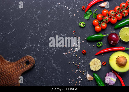 Concept of cooking healthy vegan food. Cutting board and selected vegetables, fruits, spices, herbs for making various sauces on a black stone table. Stock Photo
