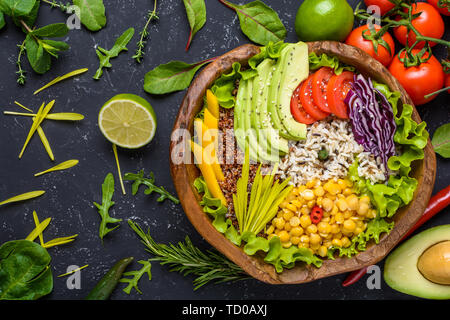 Healthy vegan superfood bowl with quinoa, wild rice, chickpea, tomatoes, avocado, greens, cabbage, lettuce on black stone background top view. Stock Photo