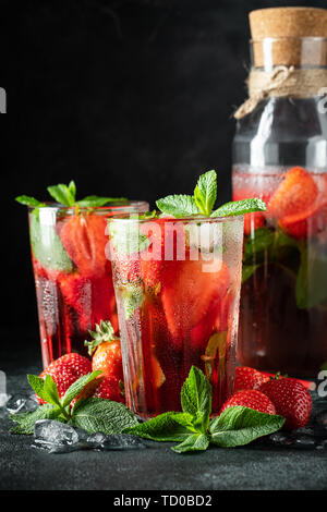 Fresh lemonade with ice, mint and strawberry on top in glass on black table background. Cold summer drink. Sparkling glasses with berry cocktail Stock Photo