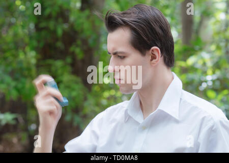 Young man is using a asthma inhaler and shaking it before Stock Photo