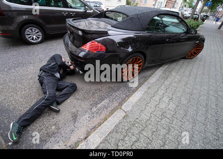 07 June 2019, Hessen, Frankfurt/Main: Nico Briesemeister uses a flashlight to check the underbody of a BMW, which the policemen in the city centre had noticed. Briesemeister is head of the police 'Control Unit Autoposer Raser Tuner' (KART), which is on the trail of racers and autoposers in the Main metropolis with civilian vehicles. The BMW was seized due to an excessive noise level caused by the manipulation of the exhaust system. (Zu dpa 'Control unit KART on tour - expensive evening for Poser') Photo: Boris Roessler/dpa Stock Photo