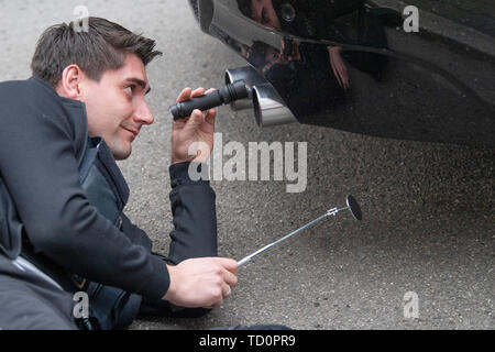 07 June 2019, Hessen, Frankfurt/Main: Police superintendent Nico Briesemeister shines a flashlight into the exhaust of a previously stopped BMW, which had attracted attention because of its loud engine noise. The vehicle has been seized. (Zu dpa 'Control unit KART on tour - expensive evening for Poser') Photo: Boris Roessler/dpa Stock Photo