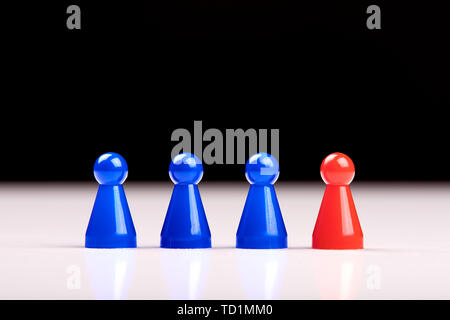 Three blue game pieces and a red figure standing next to them as a leader, boss or different. Blurred black and white background. Stock Photo