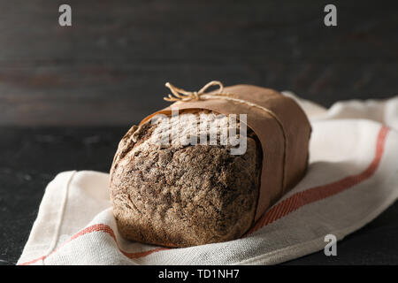 Rye bread on kitchen towel on black table against wooden background, space for text and closeup Stock Photo
