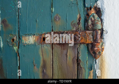 A broken rusting door hinge on a painted wooden door, paint peeling off the wood, nobody in the image Stock Photo