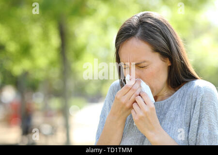 Woman sneezing using a wipe standing outdoors in a park Stock Photo