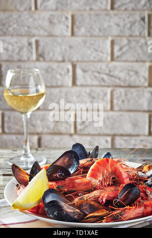 close-up of a mix of mussels, clams and king prawns with a glass of white wine and a brick wall at the background, view from above Stock Photo