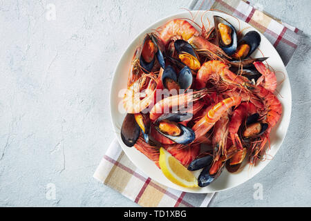 close-up of mix seafood - mussels, clams and king prawns on a white plate on a concrete table, horizontal view from above, empty space Stock Photo