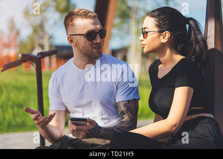 Couple of young man and woman sitting in park on wooden bench. Stock Photo