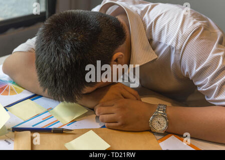 Exhausted man fall asleep on unorganized table with documents, sticky note Stock Photo