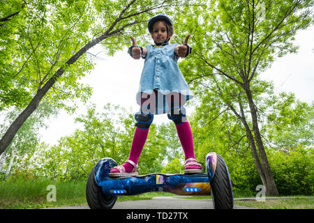 young child girl riding in a city Park on gyroscooter. Summer entertainment in nature. Electric scooter is a modern eco-friendly mode of transport Stock Photo