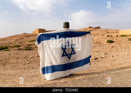 Back side of a soldier in hat holding the national flag of Israel - white with blue stripes and david's star at Masada fortification background. Young Stock Photo