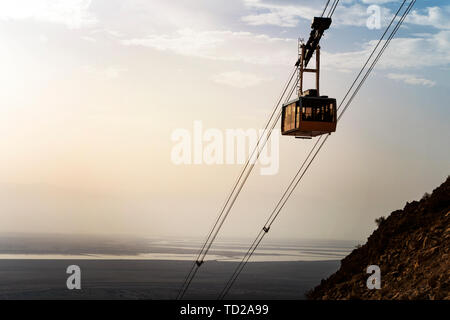 Cable car with people going down on funicular over mountains in Judean desert at the Dead sea background. Scenic view of the cable railroad with the Stock Photo