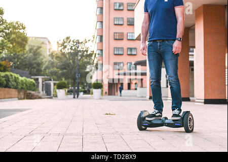 A man in jeans and sneakers on a hoverboard ride in the city. Happy boy riding around at sunset. Modern electronics for relaxation and entertainment Stock Photo