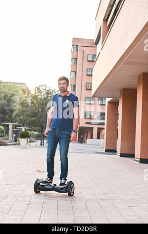 A man in jeans and sneakers on a hoverboard ride in the city. Happy boy riding around at sunset. Modern electronics for relaxation and entertainment Stock Photo