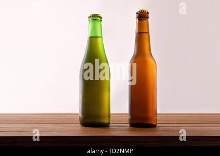 Two different beer bottles filled and closed on wooden table and light background. Horizontal composition. Front view. Stock Photo