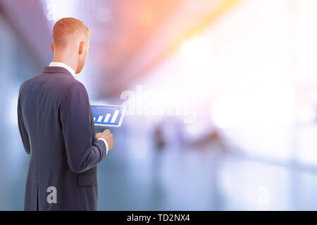 Man in suit inside an office building looking at sales forecast graphics on a tablet computer Stock Photo