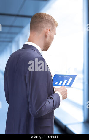 Man in suit inside an office building looking at sales forecast graphics on a tablet computer Stock Photo