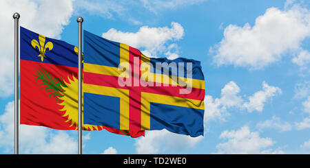 Guadeloupe and Aland Islands flag waving in the wind against white cloudy blue sky together. Diplomacy concept, international relations. Stock Photo