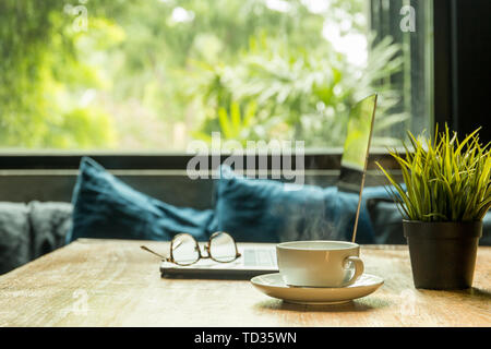 Business concept coffee cup with laptop and eyeglasses on wooden table. Stock Photo