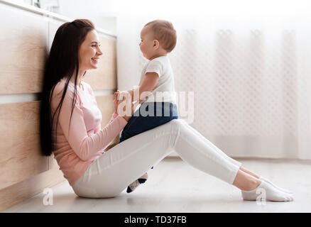 Lovely mother playing with adorable baby in kitchen Stock Photo