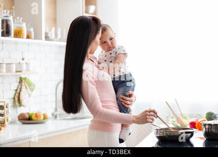 Young woman cooking with baby in kitchen Stock Photo