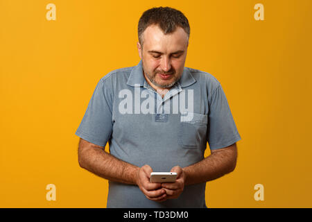Attractive young middle-aged man with smartphone on yellow background Stock Photo