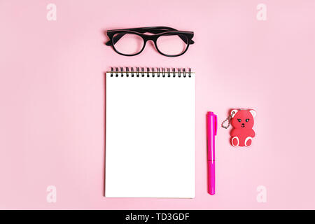 Notepad with trendy glasses and pink coral pen and toy bear gift on pastel pink background. Stock Photo
