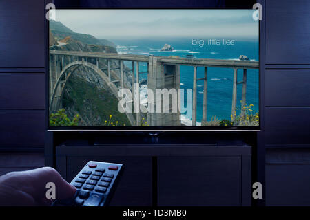 A man points a TV remote at the television which displays the Big Little Lies main title screen (Editorial use only). Stock Photo