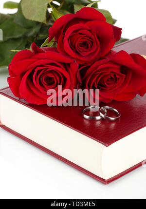 Wedding rings with roses on bible isolated on white Stock Photo