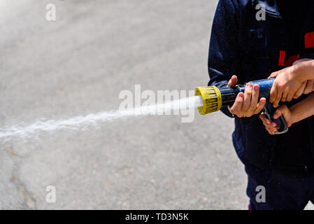 Firefighter demonstrating how to use a water hose to children during a display, helping a child hold the hose tap. Stock Photo