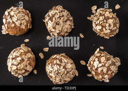 Healthy organic energy balls made with dates, oat flakes, dried cranberries, pecan nuts, over black background, flat lay. Stock Photo