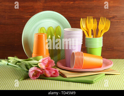Multicolored plastic tableware on table with tulips on wooden background Stock Photo