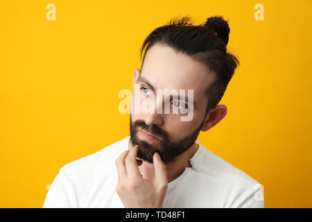 Closeup portrait of a pensive man who looks to the side, touching his chin and weighs the pros and cons of the offer, isolated on a bright yellow back Stock Photo