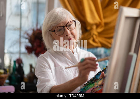 Painting in workshop. Dark-eyed aged woman painting in workshop feeling good and inspired Stock Photo