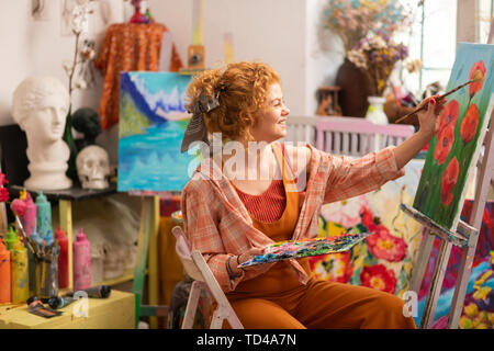Cheerful artist. Cheerful young artist wearing bright clothes feeling happy enjoying painting Stock Photo